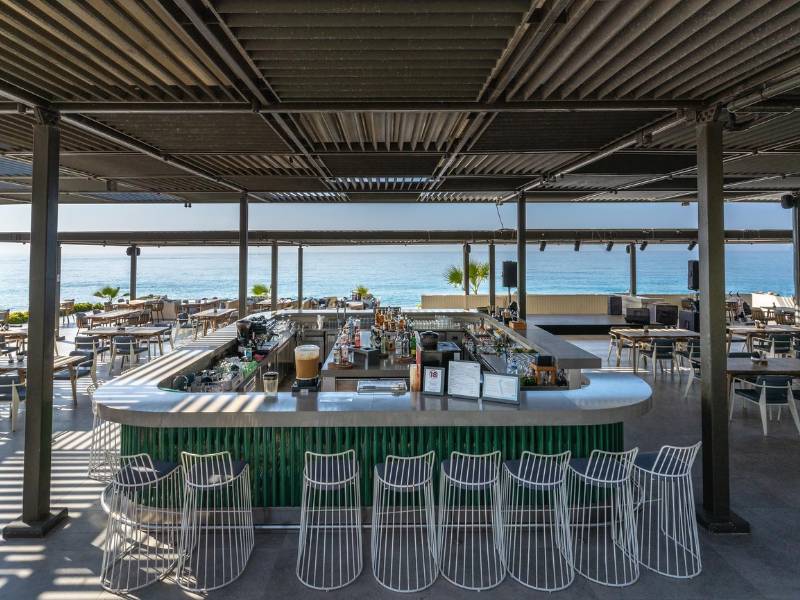 Outdoor bar with modern wire stools and beverages at Paloma Family Holidays, overlooking the ocean.