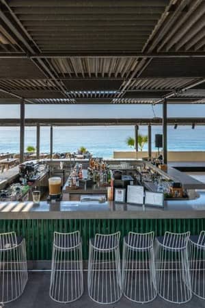 Outdoor bar with modern wire stools and beverages at Paloma Family Holidays, overlooking the ocean.