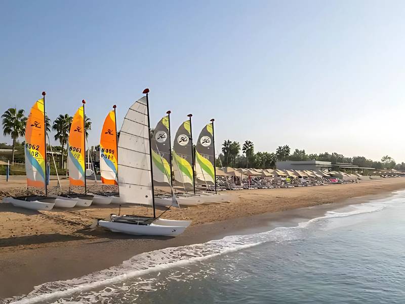 Colourful sailboats on the beach at Paloma Family Holidays resort, with palm trees and clear skies in the background.