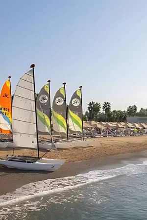 Colourful sailboats on the beach at Paloma Family Holidays resort, with palm trees and clear skies in the background.