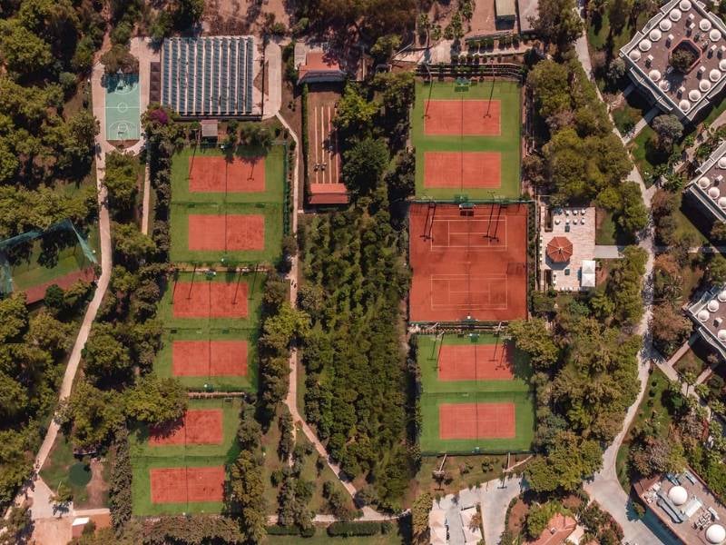 Aerial view of Paloma Gallery showing six clay tennis courts surrounded by trees and greenery.