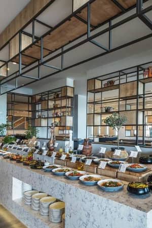 Paloma Gallery dining area showcasing modern decor, open shelving with decorative items, and an extensive buffet of dishes in stylish bowls and platters.