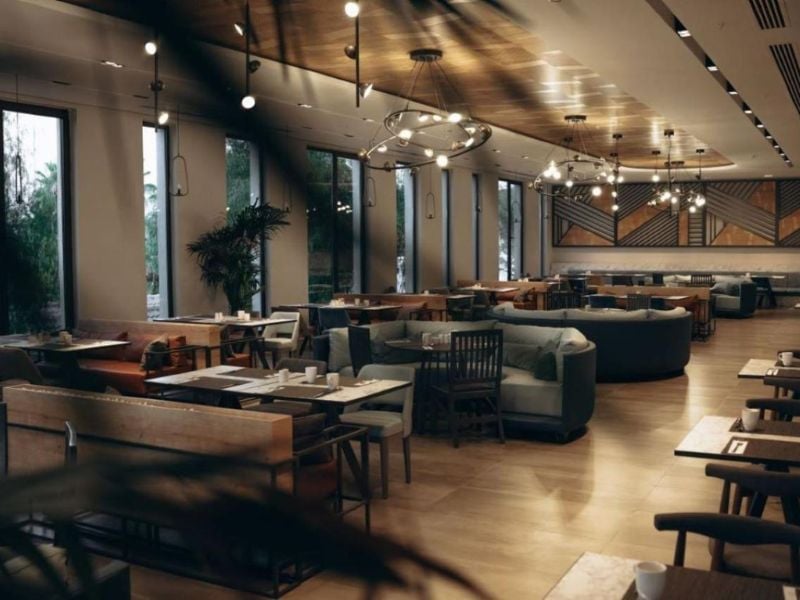 Modern lounge area in Paloma Gallery with wooden tables, sofas, large windows, and hanging lights.