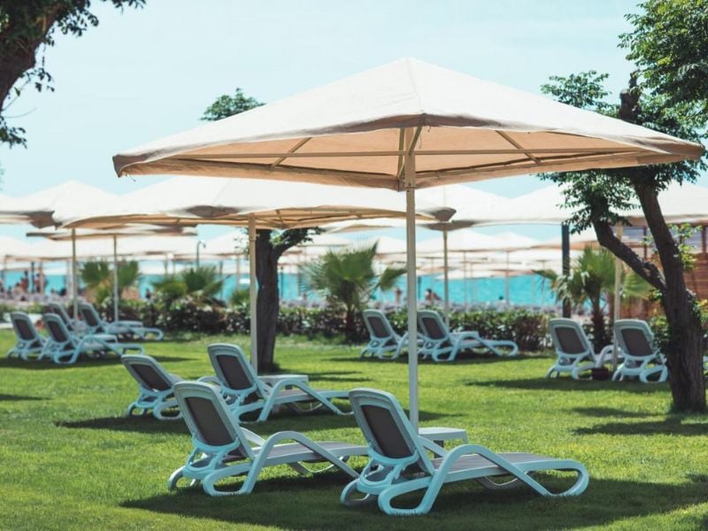 Luxurious outdoor lounging at Paloma Gallery with sun loungers under large umbrellas on a green lawn and ocean in the background.