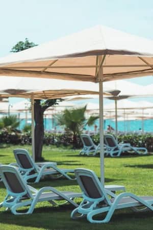 Luxurious outdoor lounging at Paloma Gallery with sun loungers under large umbrellas on a green lawn and ocean in the background.
