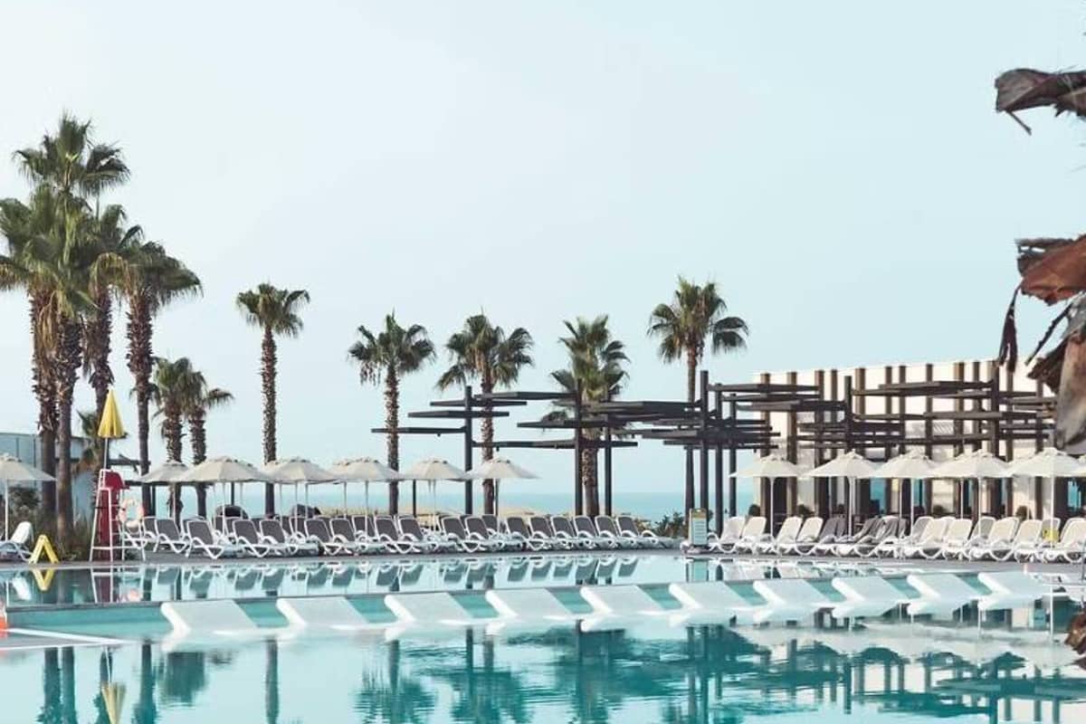 Luxurious pool area at Paloma Gallery with white sun loungers, umbrellas, and palm trees under a clear blue sky.