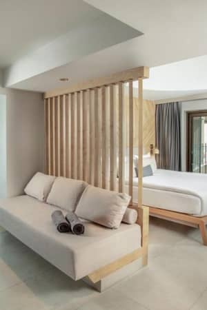 Modern hotel room at Paloma Gallery with a large bed, neutral sofa, wooden partition, and balcony overlooking gardens.