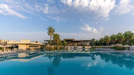 View of the Paloma Orenda resort, highlighting a large swimming pool with palm trees and resort buildings in the background.