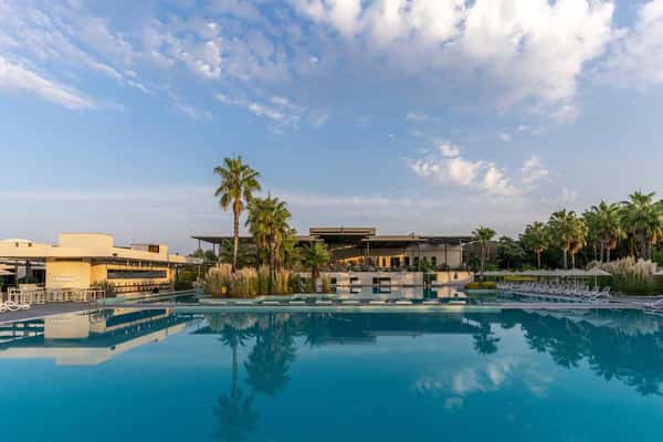 View of the Paloma Orenda resort, highlighting a large swimming pool with palm trees and resort buildings in the background.