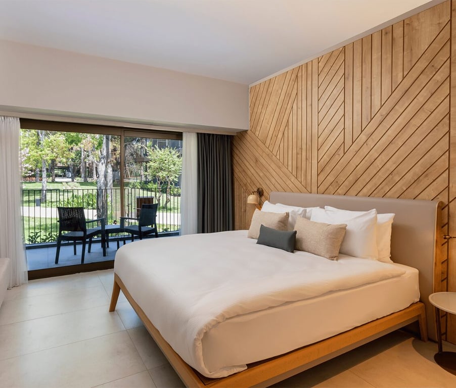 Modern hotel room at Paloma Orenda with a large bed, wooden panel wall decor, and a garden view patio accessible through a sliding glass door.