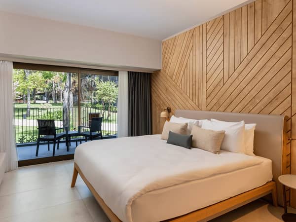 Modern hotel room at Paloma Orenda with a large bed, wooden panel wall decor, and a garden view patio accessible through a sliding glass door.