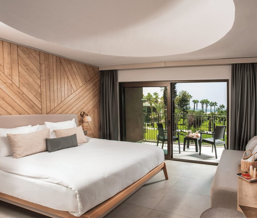 Hotel room at Paloma Orenda with a large bed, wooden decor, and a balcony offering a sea view and palm trees.