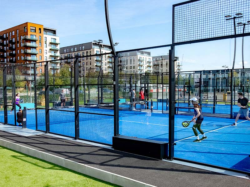 Outdoor padel court at Parkside Padel Clinic with players in action. The setting includes high-rise buildings in the background.