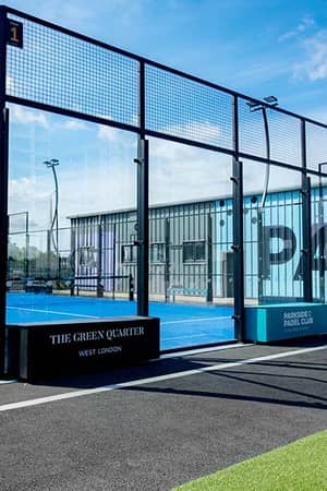 Outdoor Padel tennis court with blue surface and glass walls at Parkside Padel Club under a clear blue sky.