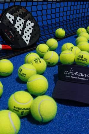 Padel court with yellow Head balls, a padel racket, and a dark blue visor marked 'activeaway | Your Tennis Experience' on a blue surface.