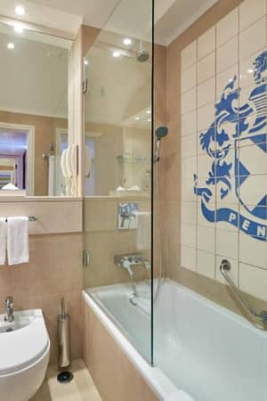 Modern bathroom at Penina Hotel with a bathtub, chrome fixtures, and the hotel's emblem on the tiled wall.