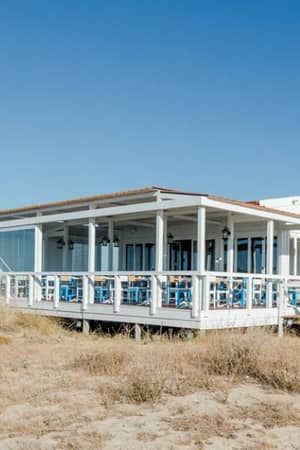 Beachfront view of Penina Hotel featuring large windows, a spacious deck, and sandy dunes under a clear blue sky.
