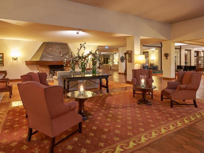 Common area of Penina Hotel with armchairs, a floral-decorated coffee table, a fireplace, and warm lighting.