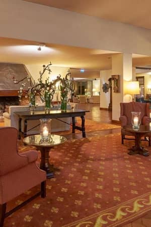 Common area of Penina Hotel with armchairs, a floral-decorated coffee table, a fireplace, and warm lighting.