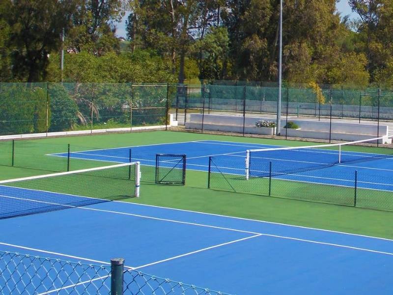 Penina Hotel tennis court with blue surface, white lines, and surrounding green fencing and trees.