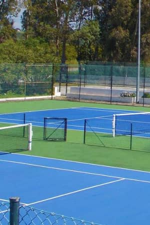 Penina Hotel tennis court with blue surface, white lines, and surrounding green fencing and trees.