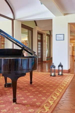 Penina Hotel lobby with a grand piano on a red carpet, surrounded by wooden decor and large windows.