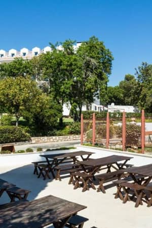 Outdoor lounge area at Penina Hotel with wooden picnic tables, trees, and tennis courts in the background.