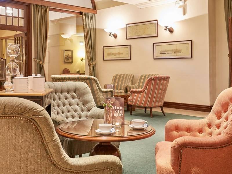 Lounge area at Penina Hotel with pastel armchairs, wooden coffee table set for tea, framed art, and soft lighting.