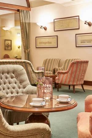 Lounge area at Penina Hotel with pastel armchairs, wooden coffee table set for tea, framed art, and soft lighting.