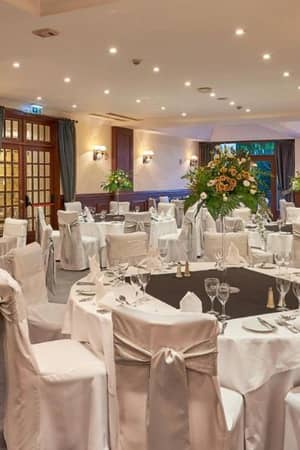 Sophisticated dining room at Penina Hotel with round tables, white tablecloths, floral centrepieces, and grey sashes on chairs, offering a stylish and elegant atmosphere.