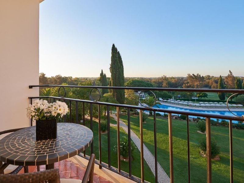Balcony view from Penina Hotel room showing a garden, a pool and a mosaic table with flowers.