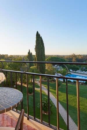Balcony view from Penina Hotel room showing a garden, a pool and a mosaic table with flowers.