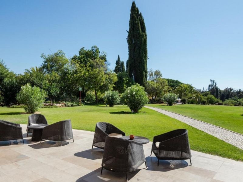Outdoor seating at Penina Hotel with wicker chairs and tables on a stone patio, overlooking green lawns and trees.