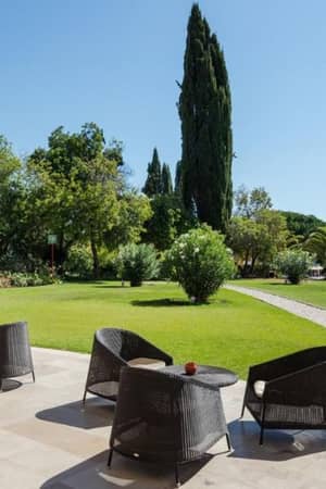 Outdoor seating at Penina Hotel with wicker chairs and tables on a stone patio, overlooking green lawns and trees.