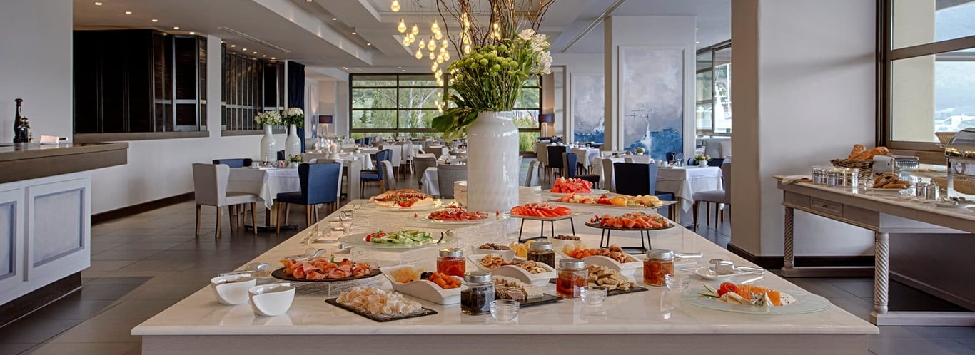 Porto Carras dining area showcasing a sophisticated buffet with an array of cheeses, meats, fruits, and condiments on a large table.