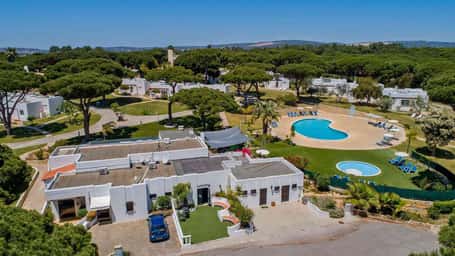 Aerial view of Prado Vilamoura hotel with pools and villas in a lush green landscape on a sunny day.