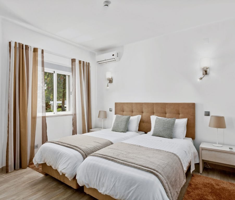 Prado Villas deluxe bedroom with two single beds, modern decor, ambient lighting, and a garden view through a large window.