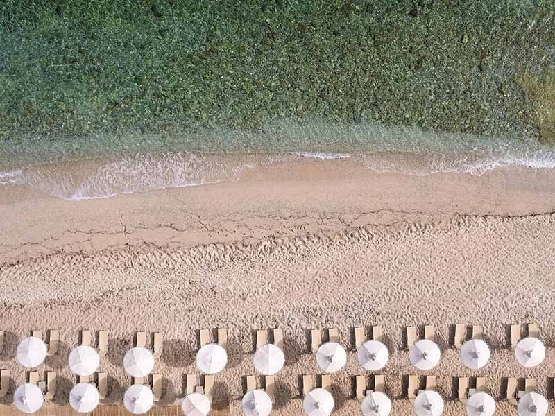 Aerial view of Royal Mare Beach featuring rows of sun loungers and white parasols, next to the turquoise sea.