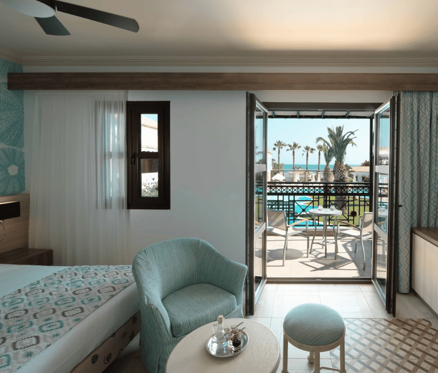 Interior of the Royal Mare Double-Twin Bungalow featuring seating, bed, and a balcony with sea views.