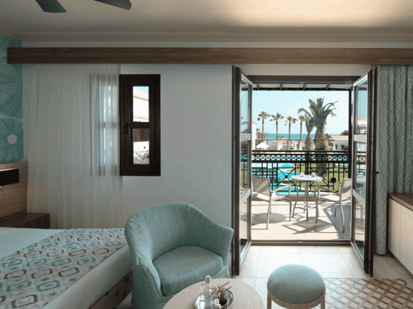 Interior of the Royal Mare Double-Twin Bungalow featuring seating, bed, and a balcony with sea views.