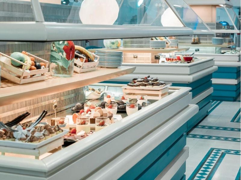 Royal Mare Gallery buffet with fresh fruits in baskets and trays of assorted desserts like pastries and cakes.