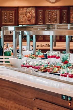 Luxurious buffet at Royal Mare Gallery with gourmet dishes, salads, drinks, and elegant presentation on a wooden counter with stainless steel warming lamps.