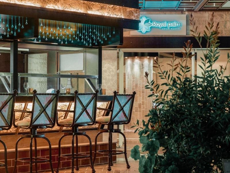 Outdoor bar at Royal Mare Gallery with stylish bar stools and Royal Palm hotel sign amidst lush greenery.