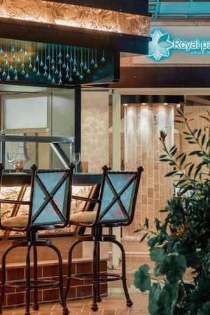 Outdoor bar at Royal Mare Gallery with stylish bar stools and Royal Palm hotel sign amidst lush greenery.