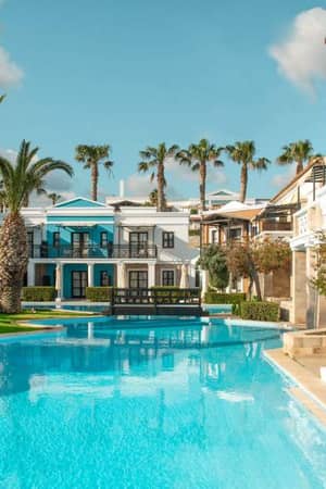 Luxurious pool at Royal Mare with palm trees and Mediterranean-style villas in the background, under a clear blue sky.