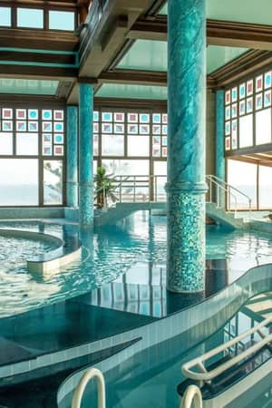 Luxurious indoor spa area at Royal Mare Gallery, featuring a large pool with mosaic columns and panoramic windows with views outside.