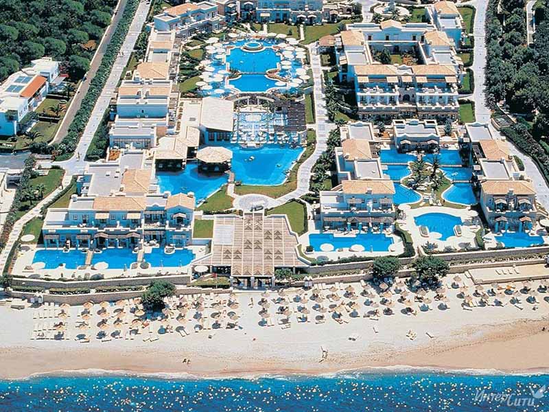 Aerial view of Aldemar Royal Mare resort in Crete, featuring multiple swimming pools, accommodation buildings, and a beachfront with loungers.