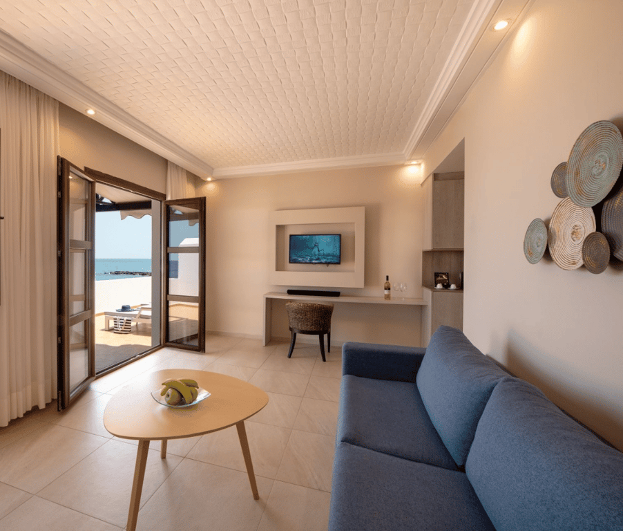Elegant interior of the Royal Mare Suite with a blue sofa, coffee table, flat-screen TV, and access to a private sea-view terrace.