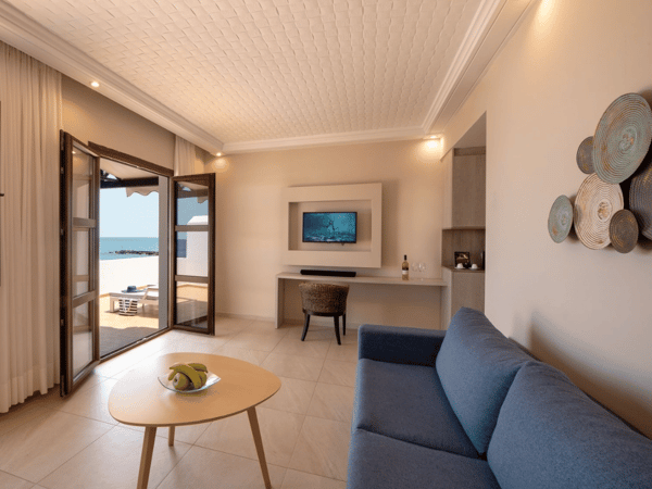 Elegant interior of the Royal Mare Suite with a blue sofa, coffee table, flat-screen TV, and access to a private sea-view terrace.