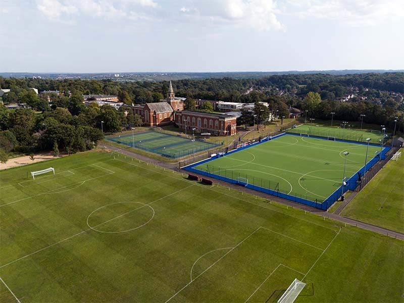 Aerial view of Royal Russell School with football pitches and tennis courts surrounded by greenery.